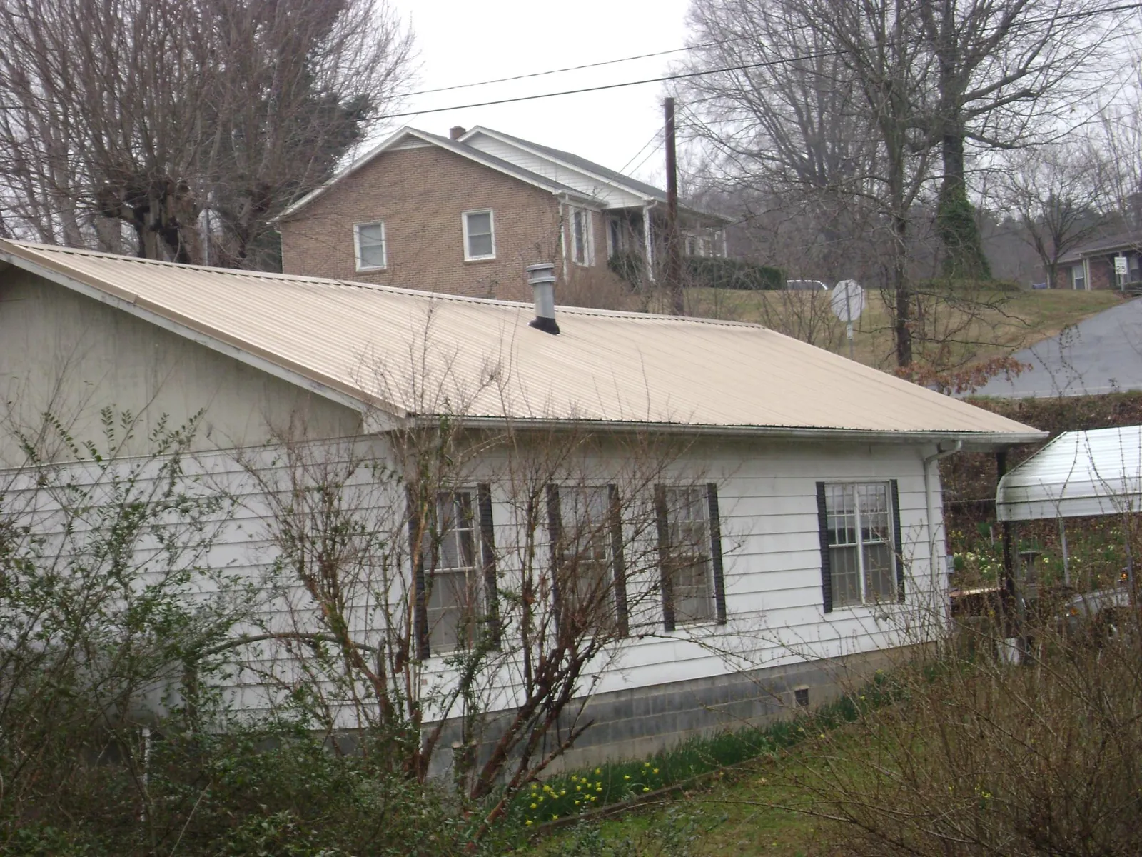 Tan metal roof on a white sided house set into a hillside — Commercial Roofing by Roofing Brothers in Brooklyn